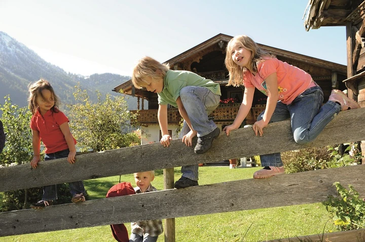 Kinder klettern gemeinsam auf einen Holzzaun