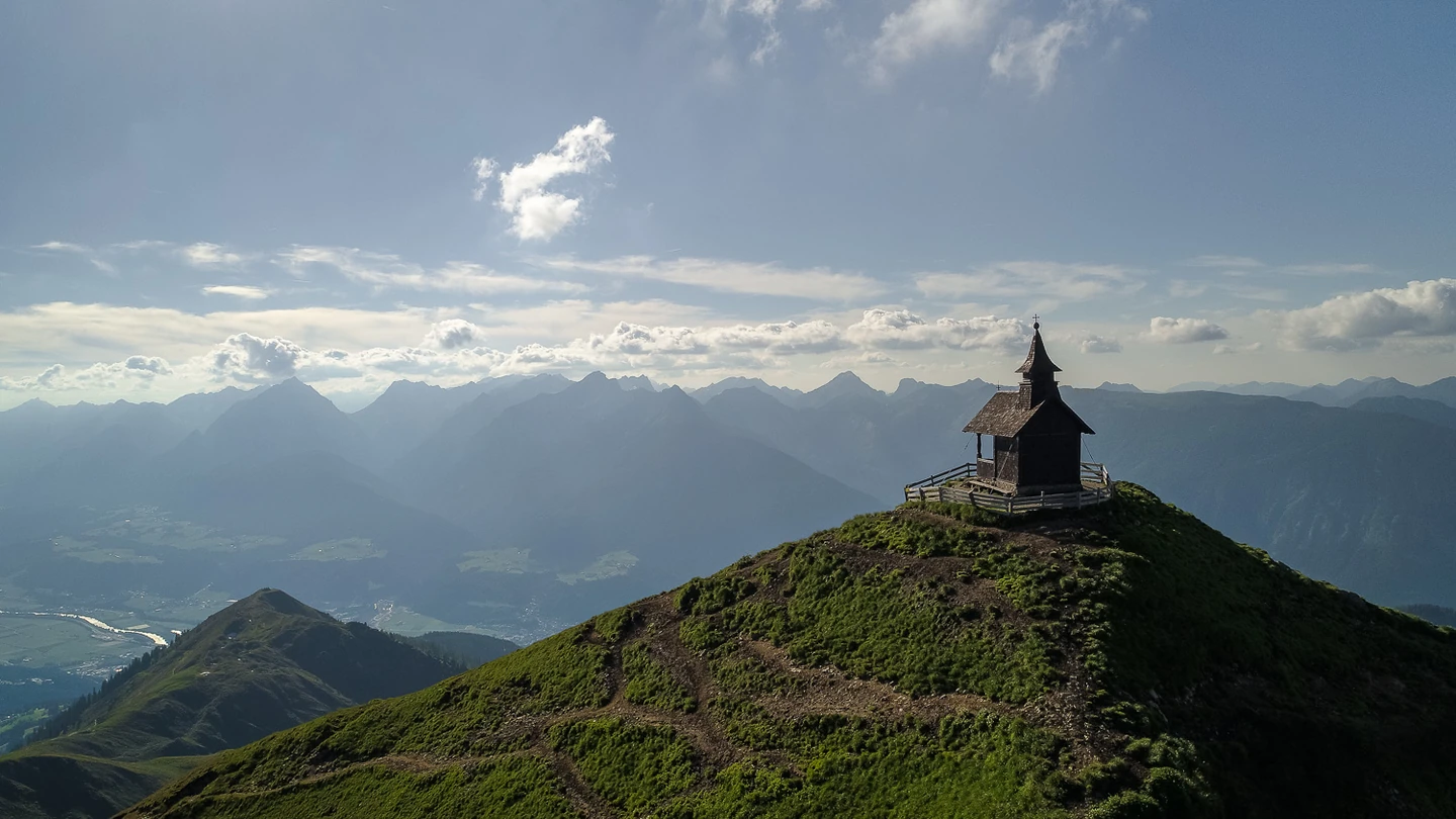 Eine kleine Bergkapelle auf einem grünen Gipfel über dem Inntal